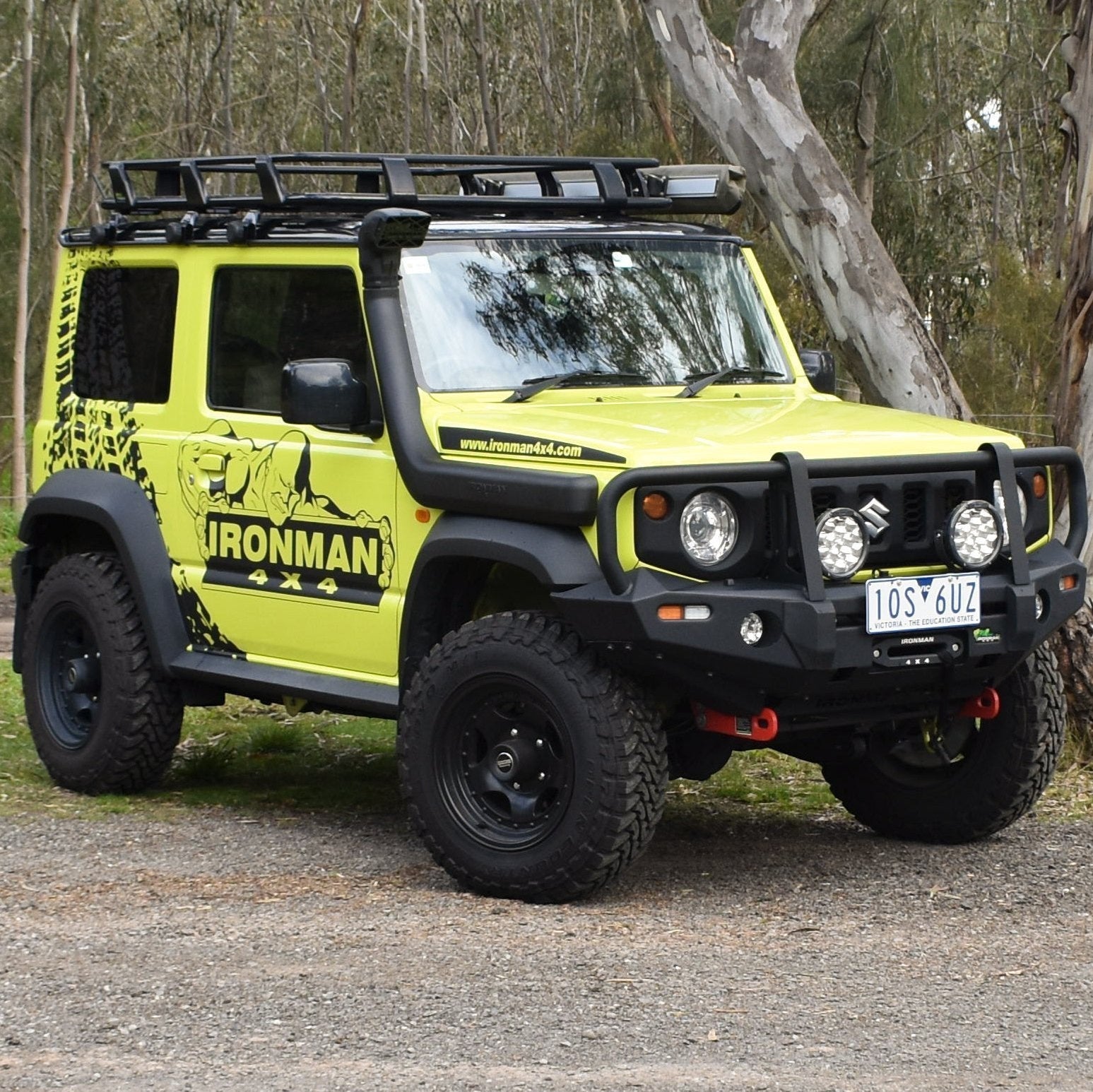 A yellow Suzuki Jimny fitted with an Ironman 4x4 snorkel, parked next to a tree.