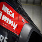 Red and black vehicle with 'MEGA JIMNY' branding on a blurred background