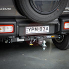 Close-up of a Suzuki jimny's hitch and license plate on a concrete surface.