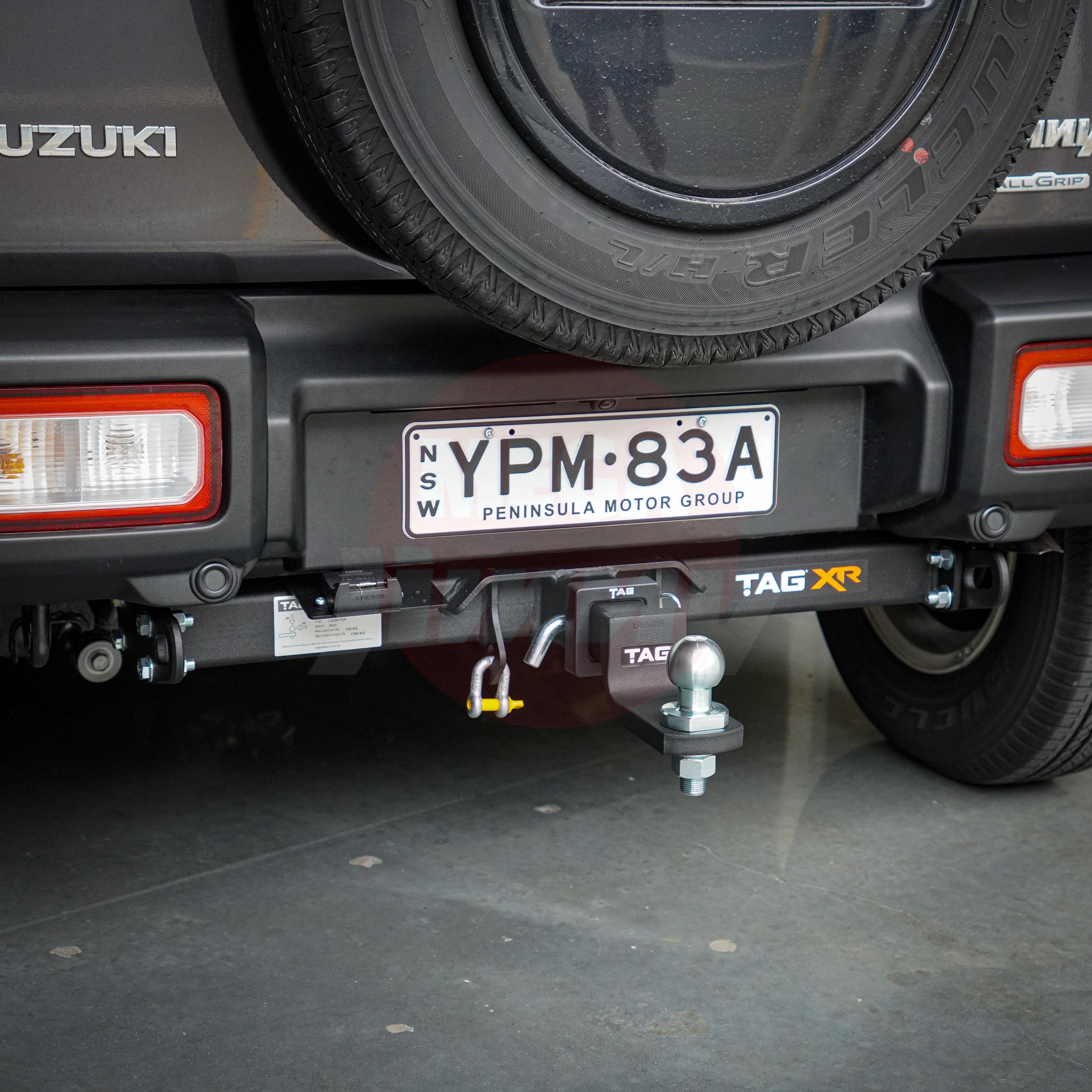 Close-up of a Suzuki jimny's hitch and license plate on a concrete surface.