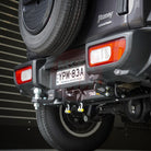 Close-up of a suzuki jimny's hitch and license plate area with a blurred background.