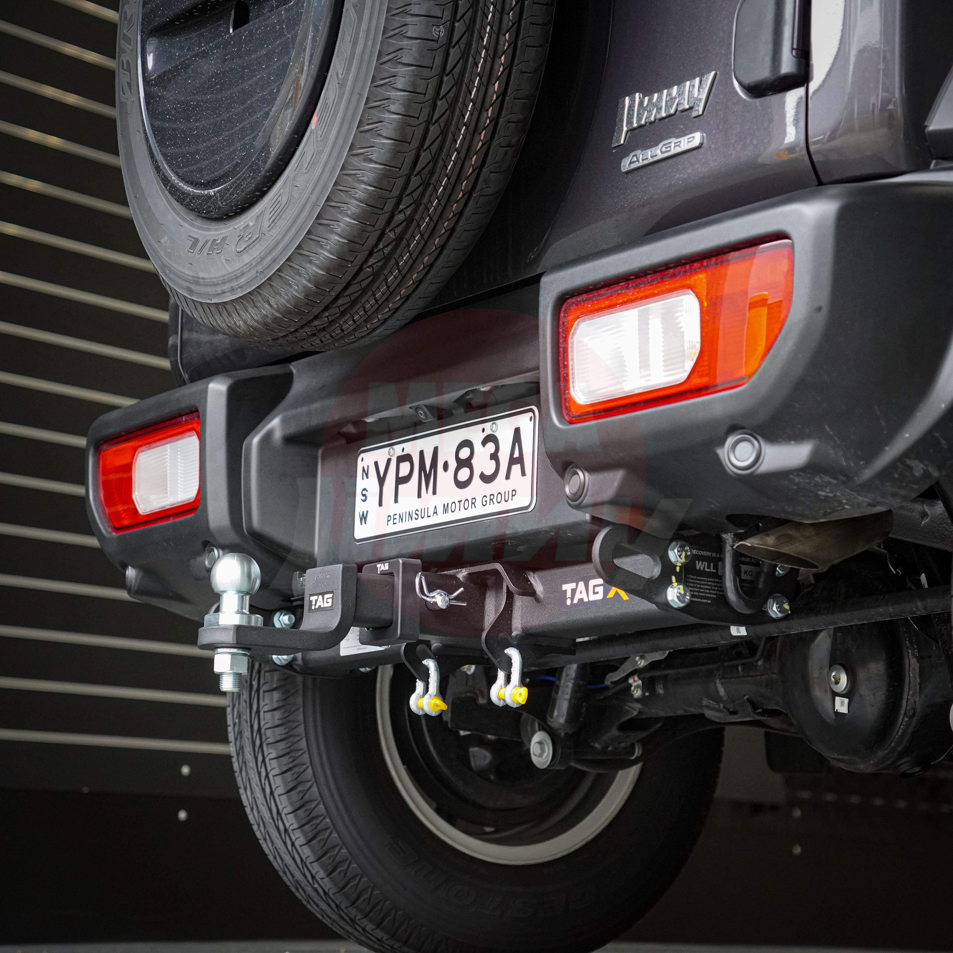 Close-up of a suzuki jimny's hitch and license plate area with a blurred background.